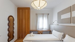 Ein Hotelzimmer mit zwei Betten, einem Holzschrank, einem Schreibtisch, einem Spiegel und einem Fenster mit Vorhängen.