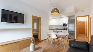 Ein modernes Wohnzimmer mit Flachbildfernseher, einem Essbereich mit Tisch und Stühlen, einer Küche mit Geräte und einer Couch.