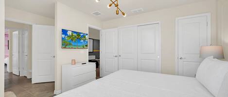 A bedroom with a large bed, white walls, a ceiling light fixture, and a painting of a beach scene.