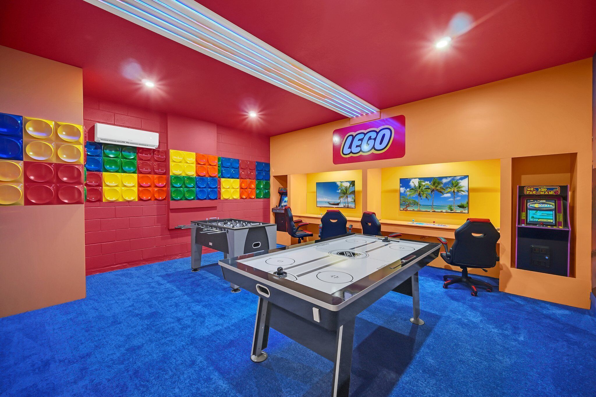 A room with a foosball table, a large LEGO sign, and a wall decorated with colorful LEGO bricks.