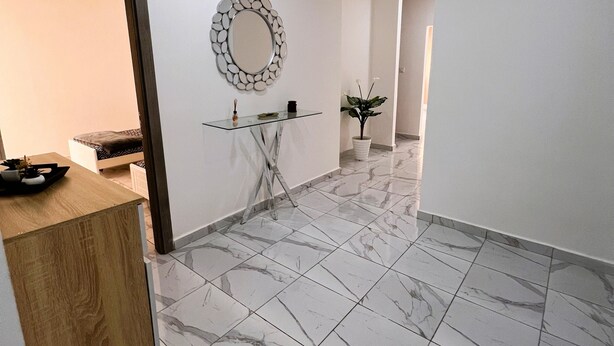 Een modern interieur met een houten receptiebalie, een console tafel met glazen blad, een marmeren vloer, een spiegel aan de muur en een kamerplant.