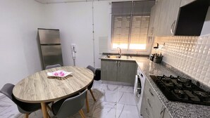 Een kleine keuken met een eethoek, een inbouwoven, een spoelbak en een raam met zonwering.