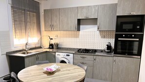 Een kleine keuken met grijze kastjes, een ingebouwde wasmachine, een magnetron en een gasfornuis.