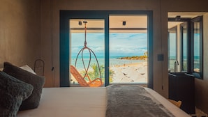 Un dormitorio con una cama grande, vista a la playa y una silla colgante.