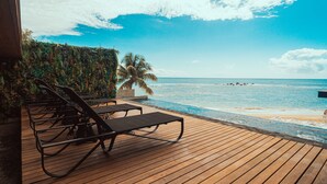 Una terraza de madera con sillones de descanso con vistas a una piscina y una playa.