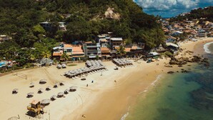 Vista aérea de una playa con una hilera de sombrillas y sillas de playa, una torre de salvavidas y edificios al fondo.