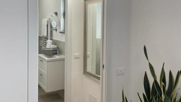 Une porte donnant sur une salle de bain équipée d’un miroir, d’un porte-serviettes et d’un lavabo.