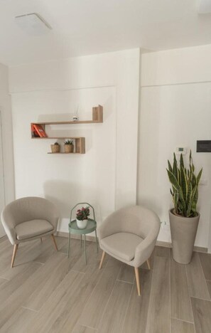 Une pièce avec deux fauteuils, une petite table sur laquelle se trouve une plante, et une plante en pot appuyée contre le mur.