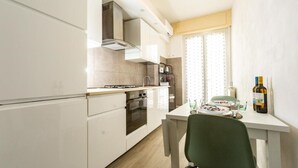 A compact kitchen with white cabinetry, a built-in oven, and a window with curtains. - Terre d'aMare Liguria (La Spezia)