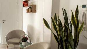 A modern living room with a beige armchair, a potted plant, and a small table with a vase. - Terre d'aMare Liguria (La Spezia)