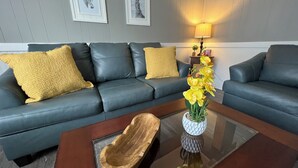 Un salon moderne avec un canapé bleu foncé, deux coussins décoratifs jaunes, une table basse en bois et un vase rempli de fleurs jaunes.