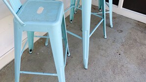 Une petite table en métal bleu clair et deux chaises assorties. Sur la table, on trouve un panier tressé contenant des fruits et des feuilles.