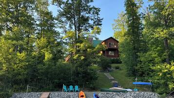 Une cabane entourée d’une forêt dense, une jetée avec des chaises et des kayaks.