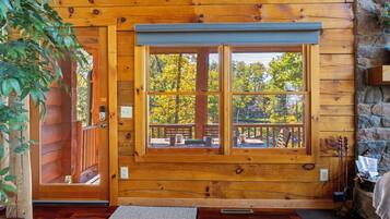 L’intérieur d’un chalet en bois, avec une grande fenêtre, des murs en bois et une cheminée en pierre.