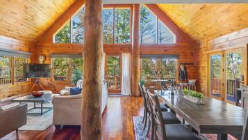 Une cabane en bois spacieuse, dotée d’un grand espace repas, d’un coin salon confortable et de grandes fenêtres offrant une vue sur la forêt environnante.