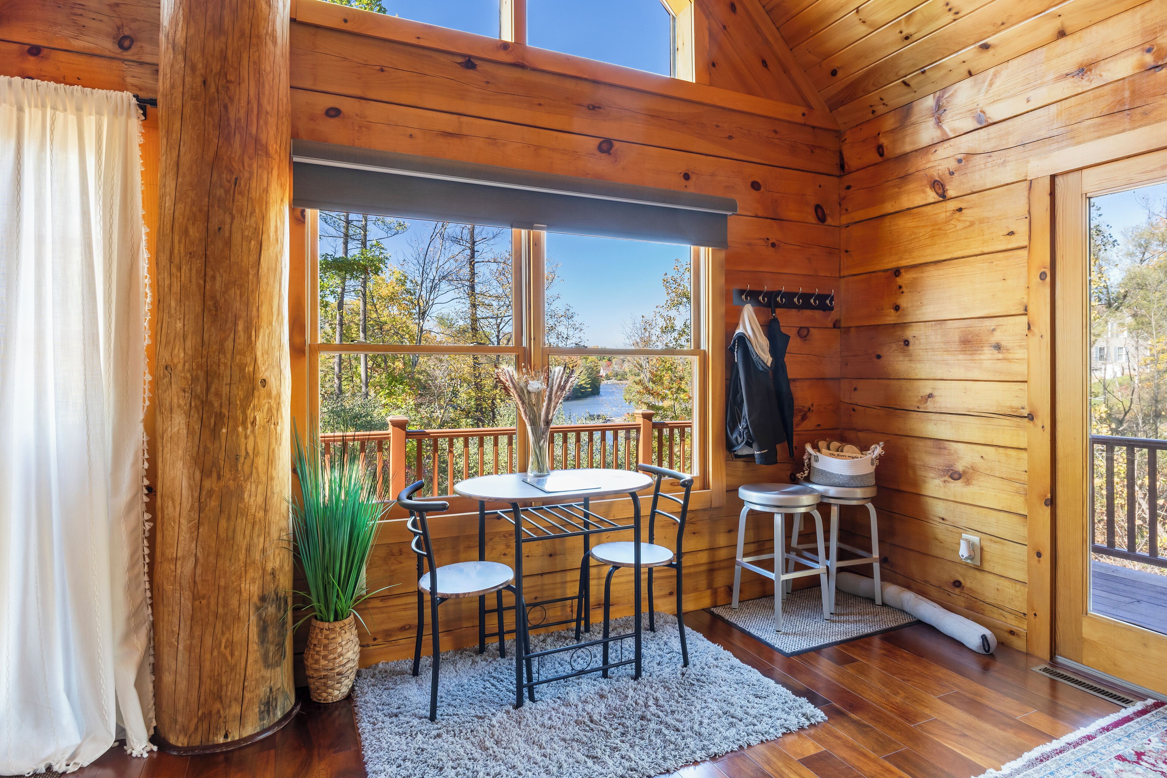 A wooden cabin with a dining area featuring a table and chairs, a potted plant, and a view of the outdoors.