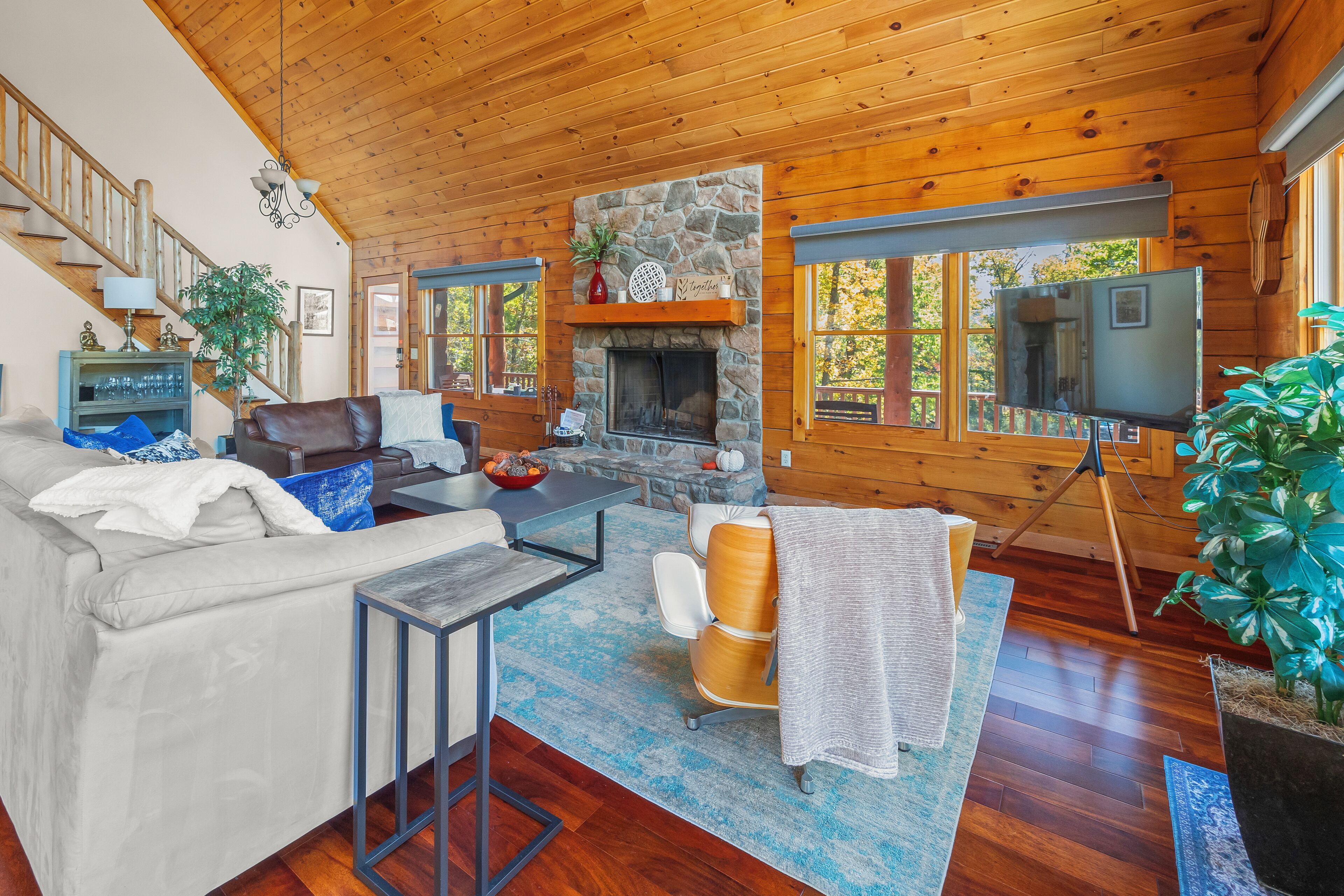 L’intérieur chaleureux d’un chalet avec une cheminée en pierre, un plafond en bois et une grande fenêtre donnant sur une forêt.