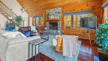 L’intérieur chaleureux d’un chalet avec une cheminée en pierre, un plafond en bois et une grande fenêtre donnant sur une forêt.