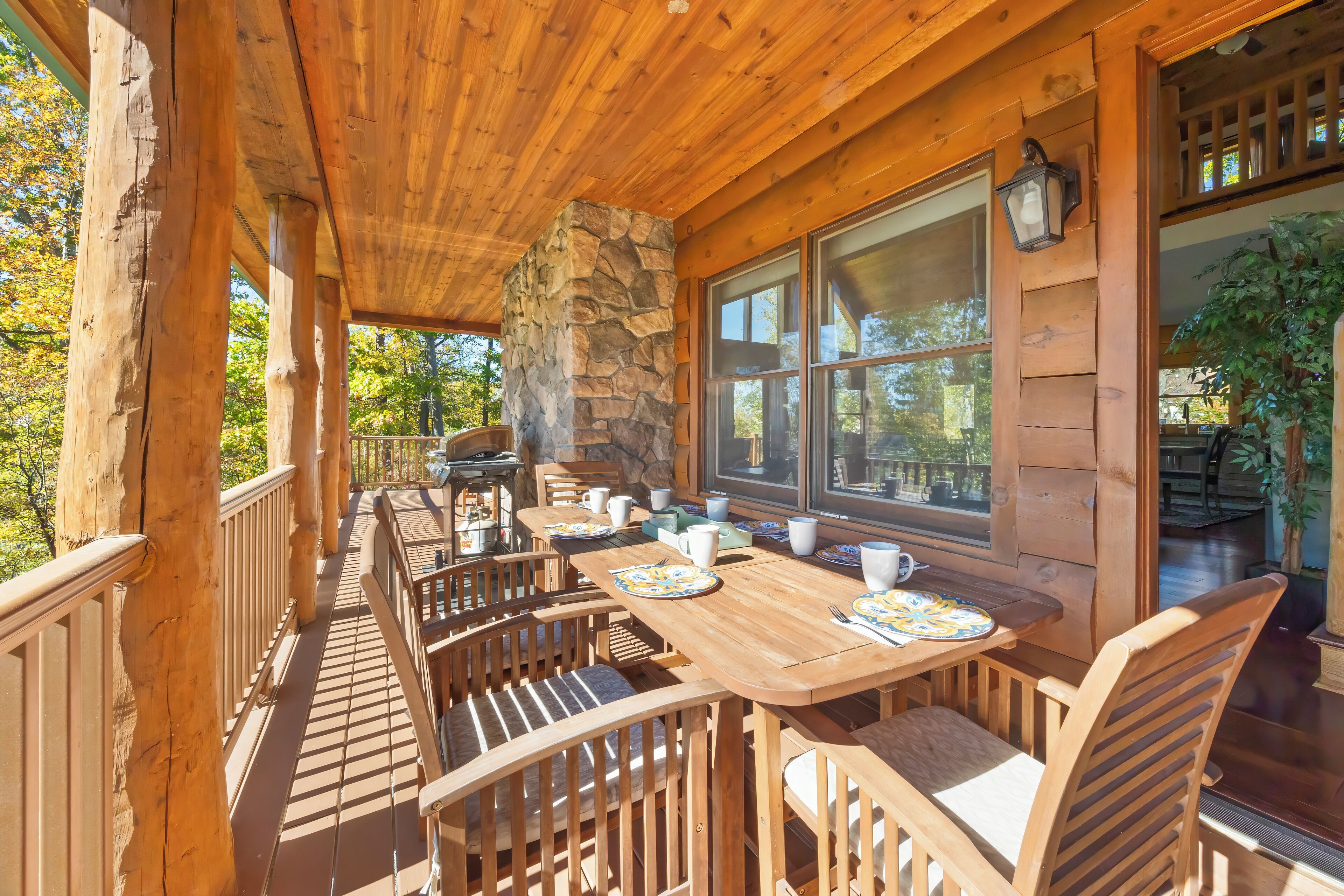 A wooden deck with a stone pillar, wooden chairs, and a table set for dining.