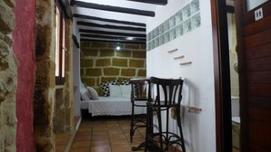 A narrow hallway with a stone wall, a bed with a white bedspread, a wooden chair, and a tiled floor. - Authentic Escape: Tosca Stone Studio in Javea (Xàbia)