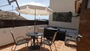 A rooftop terrace with a round table, four chairs, a white umbrella, and a decorative wall panel. - Authentic Escape: Tosca Stone Studio in Javea (Xàbia)