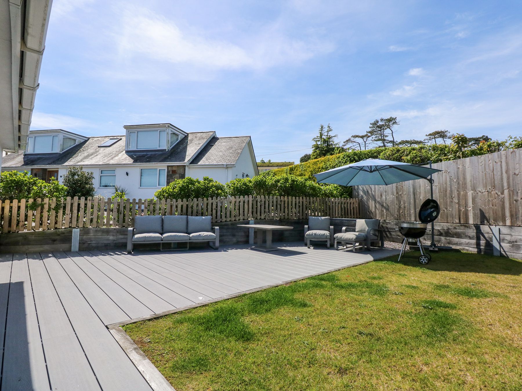A backyard with a wooden deck, a sofa, a table, and a barbecue grill.