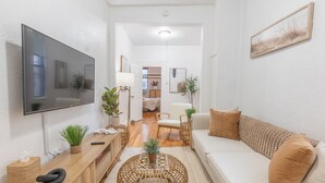 A modern living room with a flat-screen TV, a sofa, a coffee table, and a dining area in the background. - Spring 25% Discount is here, 1King bed, Near NYC (Hoboken)