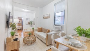 A modern living room with a sofa, dining table, and chairs. There is a television mounted on the wall and a window with blinds. - Spring 25% Discount is here, 1King bed, Near NYC (Hoboken)