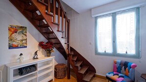 A staircase leading to a loft bedroom with a large window, a colorful armchair, and a white console table with shelves.