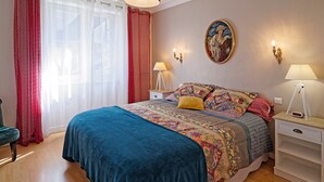 A bedroom with a large bed, two bedside tables, a chair, and a window with curtains.