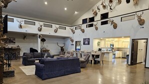 A spacious living area with a large blue sofa, a dining table with chairs, and a kitchen in the background. - Spacious modern lodge outside of city (Grand Island)
