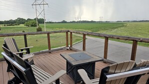 A wooden deck with Adirondack chairs and a small table, overlooking a green field and power lines. - Spacious modern lodge outside of city (Grand Island)