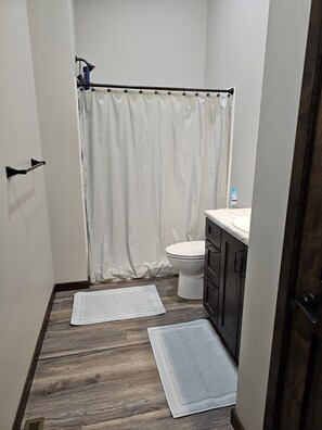 Une salle de bain avec un rideau de douche, des toilettes, un lavabo et deux tapis sur le sol.