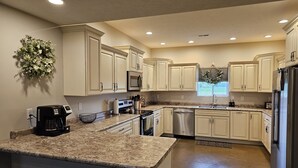 A modern kitchen with white cabinets, granite countertops, stainless steel appliances, and a built-in dishwasher. - Spacious modern lodge outside of city (Grand Island)