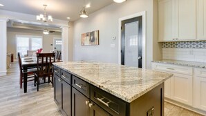 A kitchen with granite countertops, white cabinets, and pendant lighting.