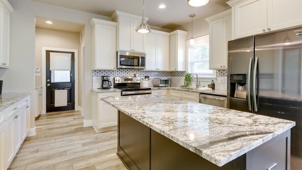 A modern kitchen with white cabinets, stainless steel appliances, and a marble countertop.