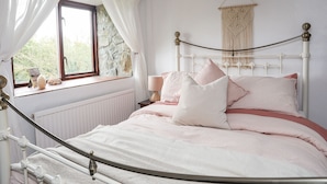 Un dormitorio con cama, ventana con cortinas, pared de piedra y un tapiz de macramé.
