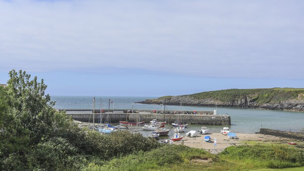 Un puerto costero con barcos amarrados, un muelle y un paisaje rocoso al fondo.