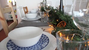 Una mesa de comedor dispuesta con platos blancos, cuencos con diseño azul, vasos transparentes y un adorno navideño de pino con luces.