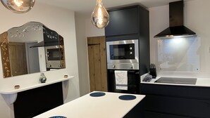 Eine moderne Küche mit Einbauofen, Mikrowelle und einer schwarzen Dunstabzugshaube. Eine weiße Arbeitsplatte mit einer blauen Schüssel und einem Spiegel darüber.