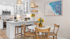 Une cuisine moderne avec des meubles blancs, un îlot central et un coin repas doté de chaises en bois.