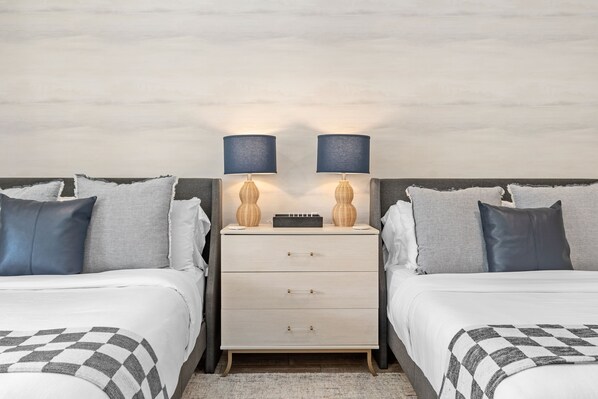 A hotel room with two beds, a nightstand with lamps, and a check-in counter.