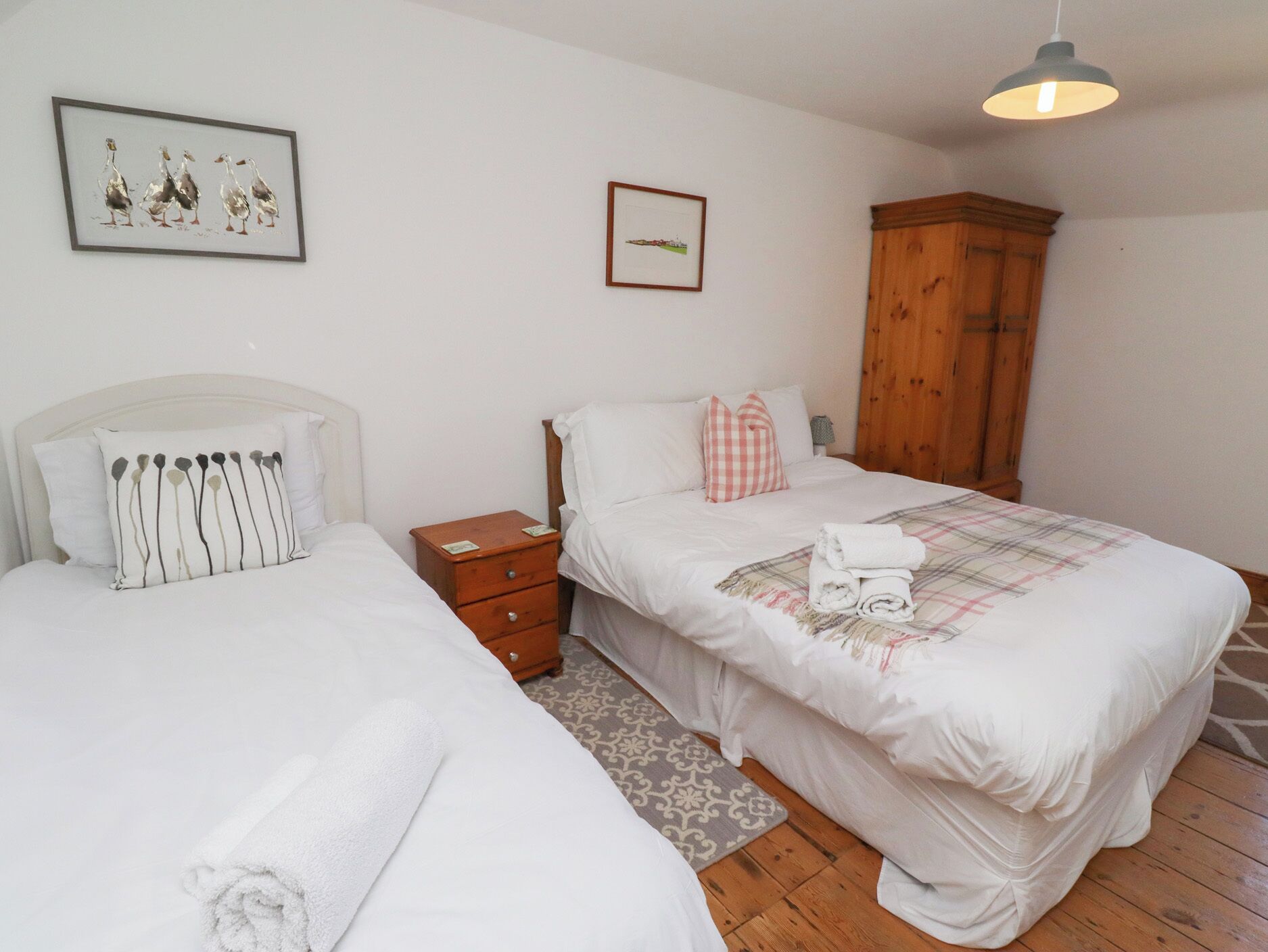 Een slaapkamer met twee eenpersoonsbedden, een houten garderobe, een nachtkastje en een lijst met een foto aan de muur.
