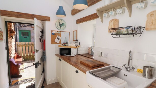 Una cocina compacta con encimera de madera, un lavamanos blanco y una lámpara colgante azul.