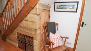 Una escalera de madera conduce a un dormitorio tipo altillo con chimenea empotrada. Una mecedora con cojín a cuadros está apoyada contra la pared.