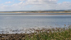 Eine Küstenlandschaft mit ruhigem Meer, Sanddünen und einer felsigen Küste.