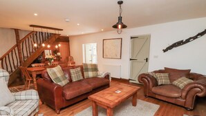 Ein gemütliches Wohnzimmer mit einer Holztreppe, Ledersofas, einem Couchtisch aus Holz und einem Essbereich mit einem Holztisch und Stühlen.