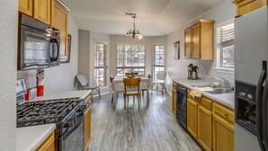 Una cocina con armarios de madera, estufa a gas, refrigerador y comedor con mesa y sillas.