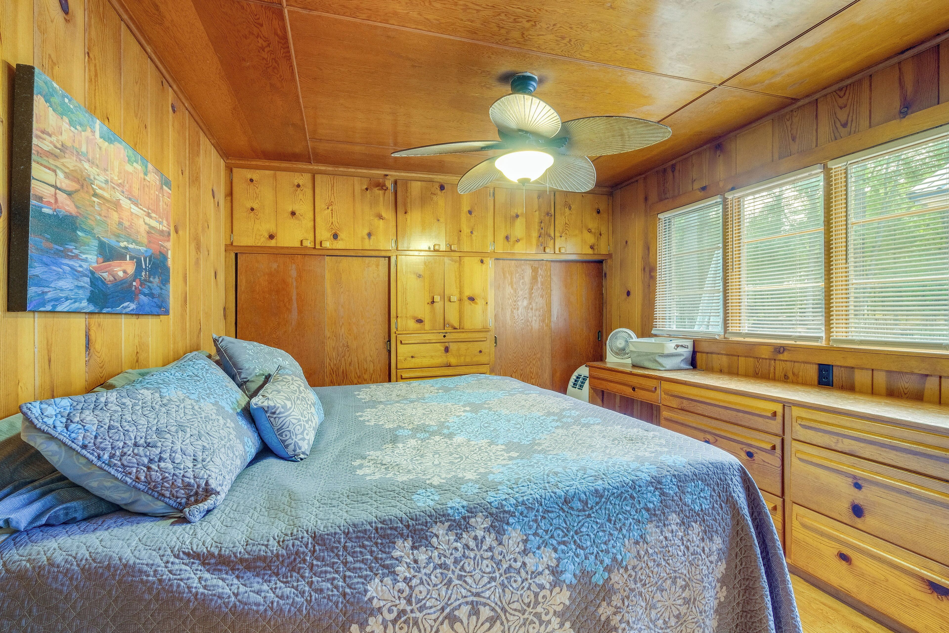 A wooden cabin room with a bed, wooden cabinets, a ceiling fan, and a window with blinds.