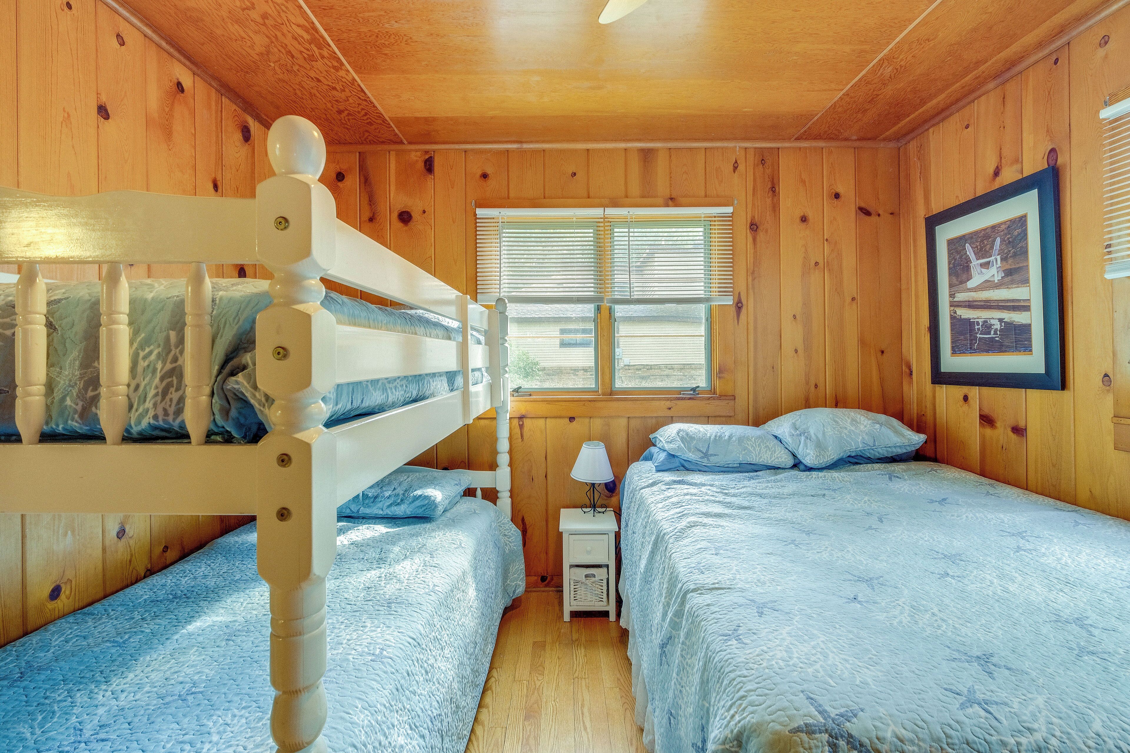 A wooden cabin room with two beds, a nightstand, and a window with blinds.